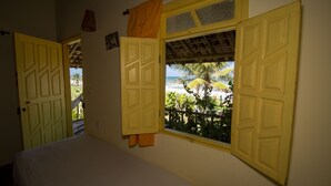 A room with a bed, a window with shutters, and a view of the beach. - Casa ImBale (Mata de São João)