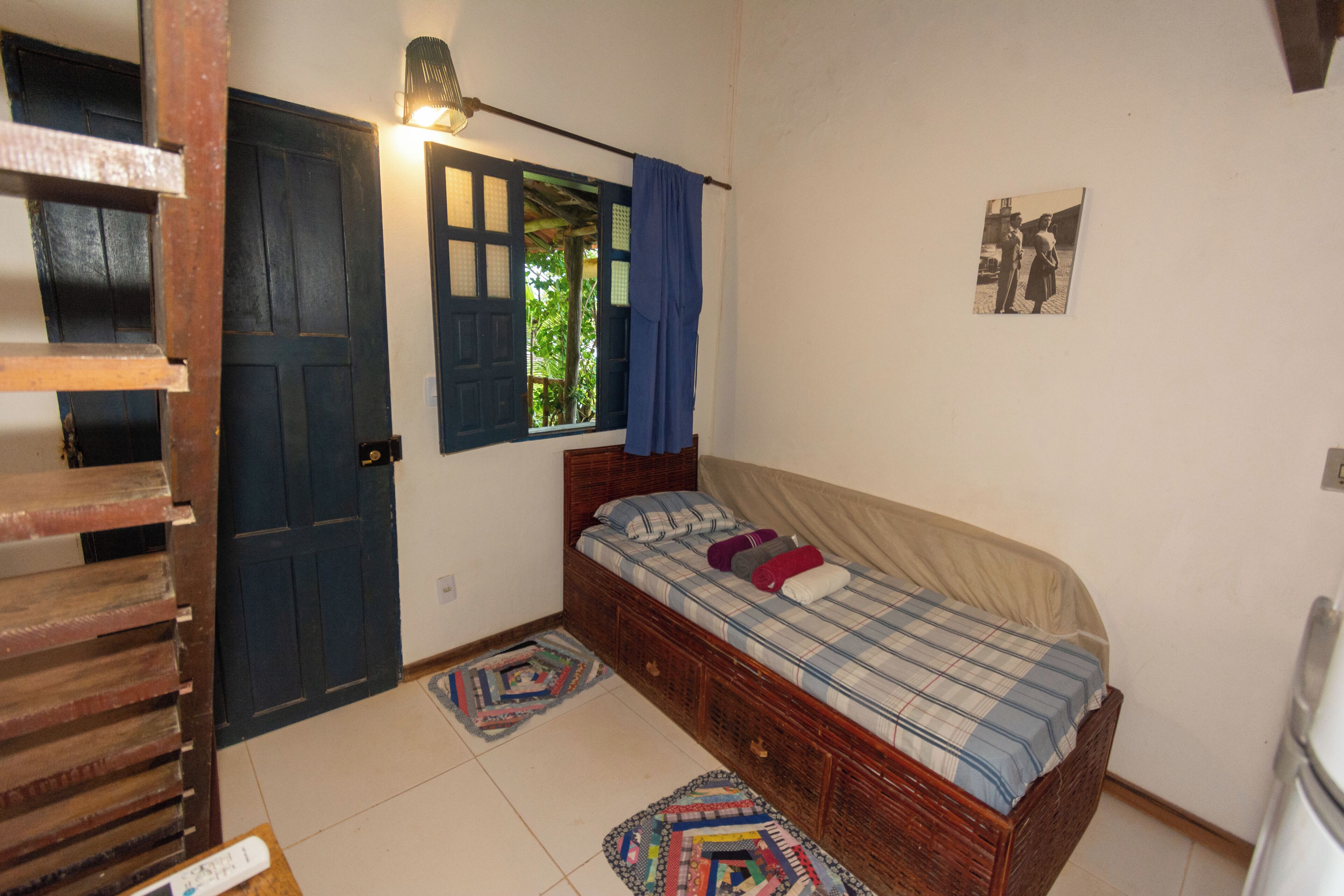 A small, cozy bedroom with a wooden bed, a window with blue curtains, and a door.