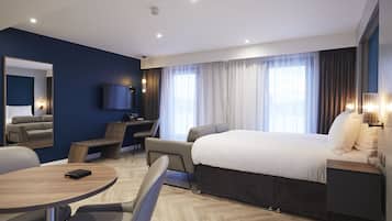 A modern hotel room with a large bed, a desk, a chair, a round table, and a TV.