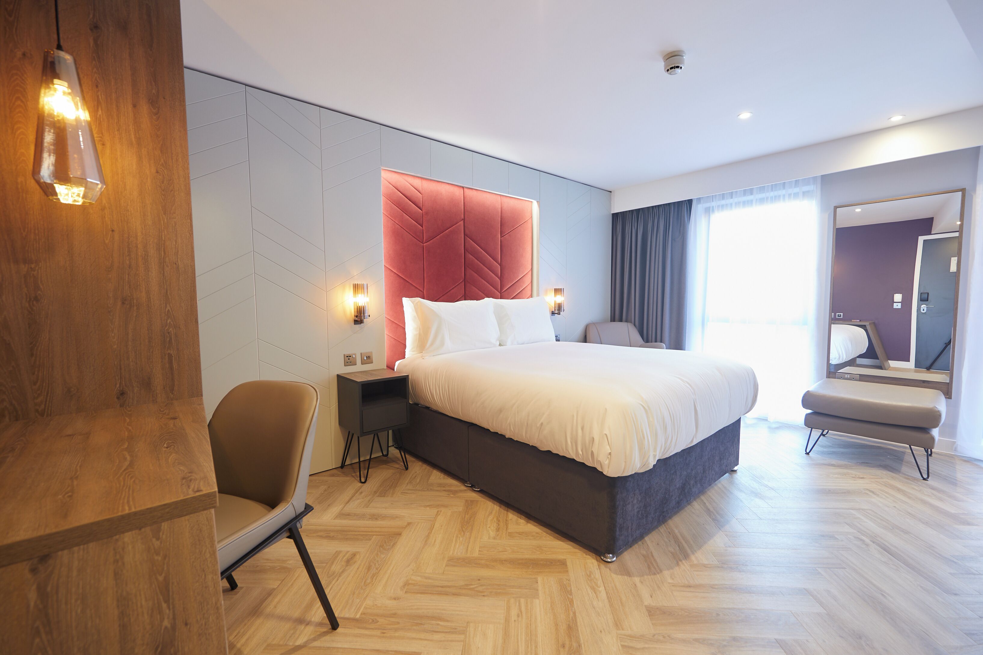 Una habitación de hotel moderna con una cama grande, suelo de madera, una zona de estar y un espejo.