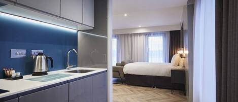 Una habitación de hotel moderna con kitchenette, una cama y una mesita de noche, y vistas a la ciudad.