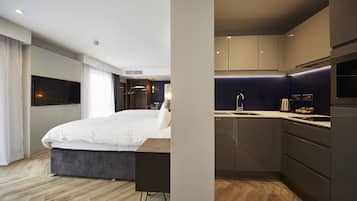 Una habitación de hotel moderna con una cama grande, un escritorio, un televisor de pantalla plana y una kitchenette.