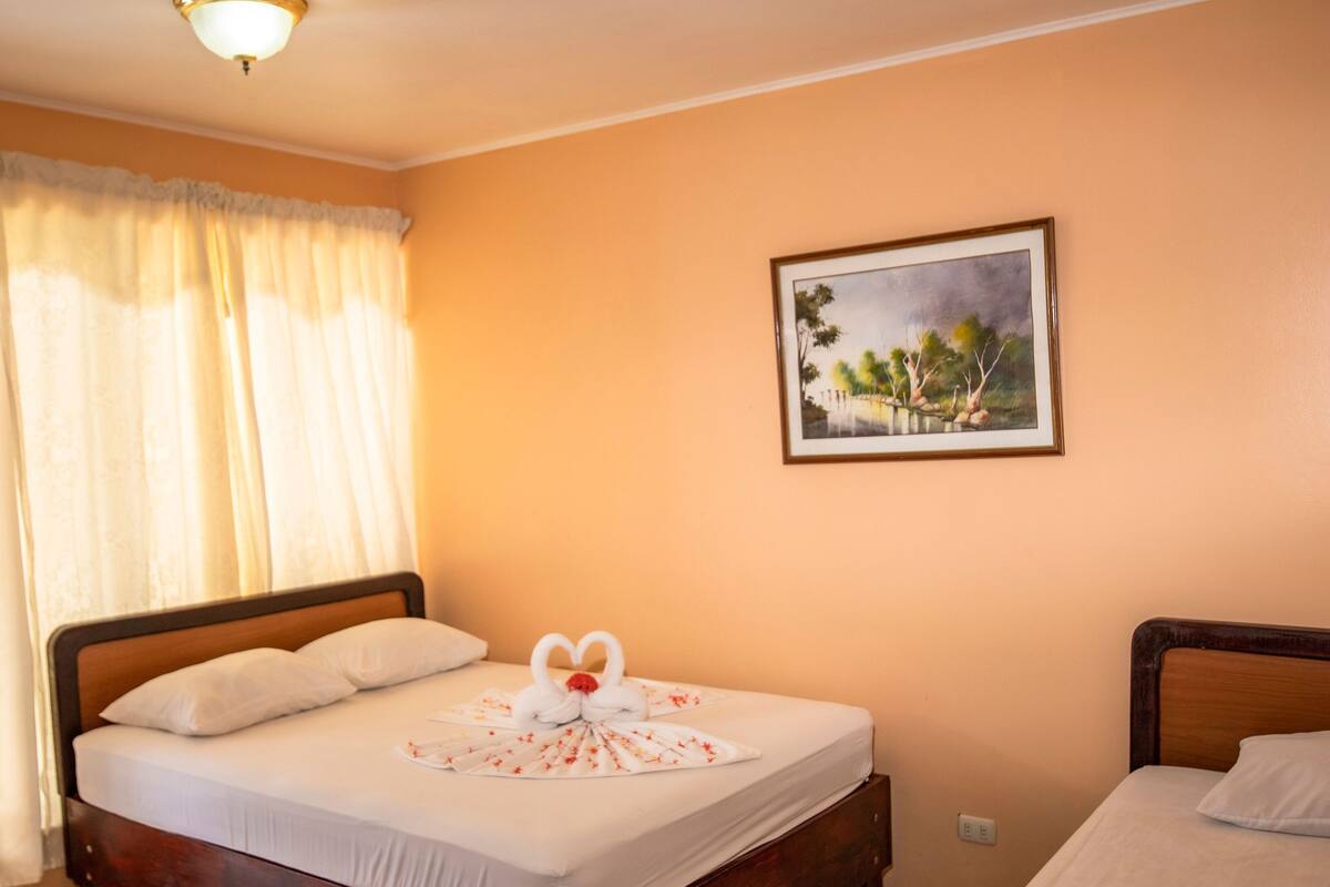 Hotelkamer met een bed, nachtkastje, een lijst met afbeelding aan de muur en een raam met gordijnen.