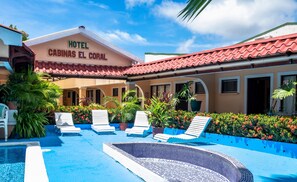 Un hotel llamado 'Cabinas El Coral' con piscina, sillones de descanso y plantas tropicales.