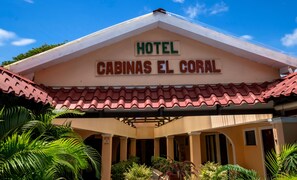 Un hotel llamado 'Cabinas El Coral' con techo de tejas rojas y un área de entrada cubierta con plantas.