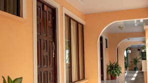A hallway with a tiled floor, a wooden door, and potted plants. - Hotel y Cabinas El Coral (Jacó)