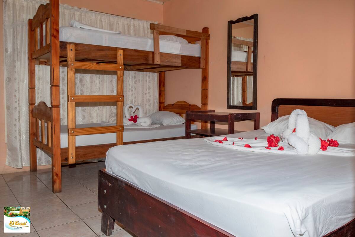 Een hotelkamer met een stapelbed, een enkel bed, een houten nachtkastje en een spiegel.