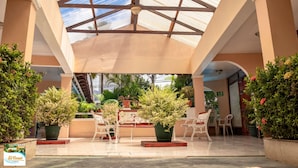 A covered outdoor area with potted plants, white chairs, and a staircase. - Hotel y Cabinas El Coral (Jacó)
