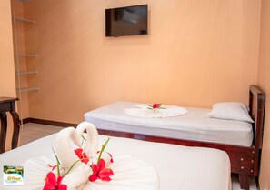 Una habitación de hotel con dos camas, un televisor montado en la pared y una silla de madera.