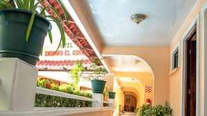 A corridor with potted plants, a tiled floor, and a building with a sign reading "CABINAS EL CORONADO". - Hotel y Cabinas El Coral (Jacó)