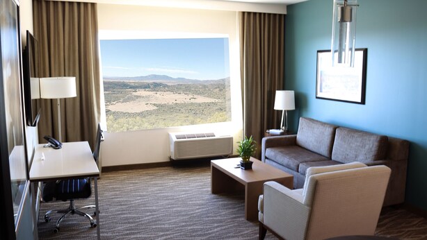 A hotel room with a desk, chair, couch, and a large window offering a view of a desert landscape.