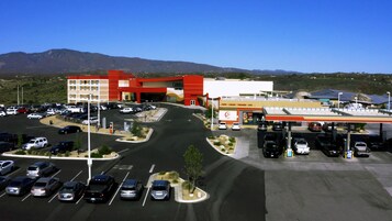 Ein Parkplatz mit mehreren Autos, ein Gebäude mit roter und gelber Fassade sowie eine gebirgige Landschaft im Hintergrund.