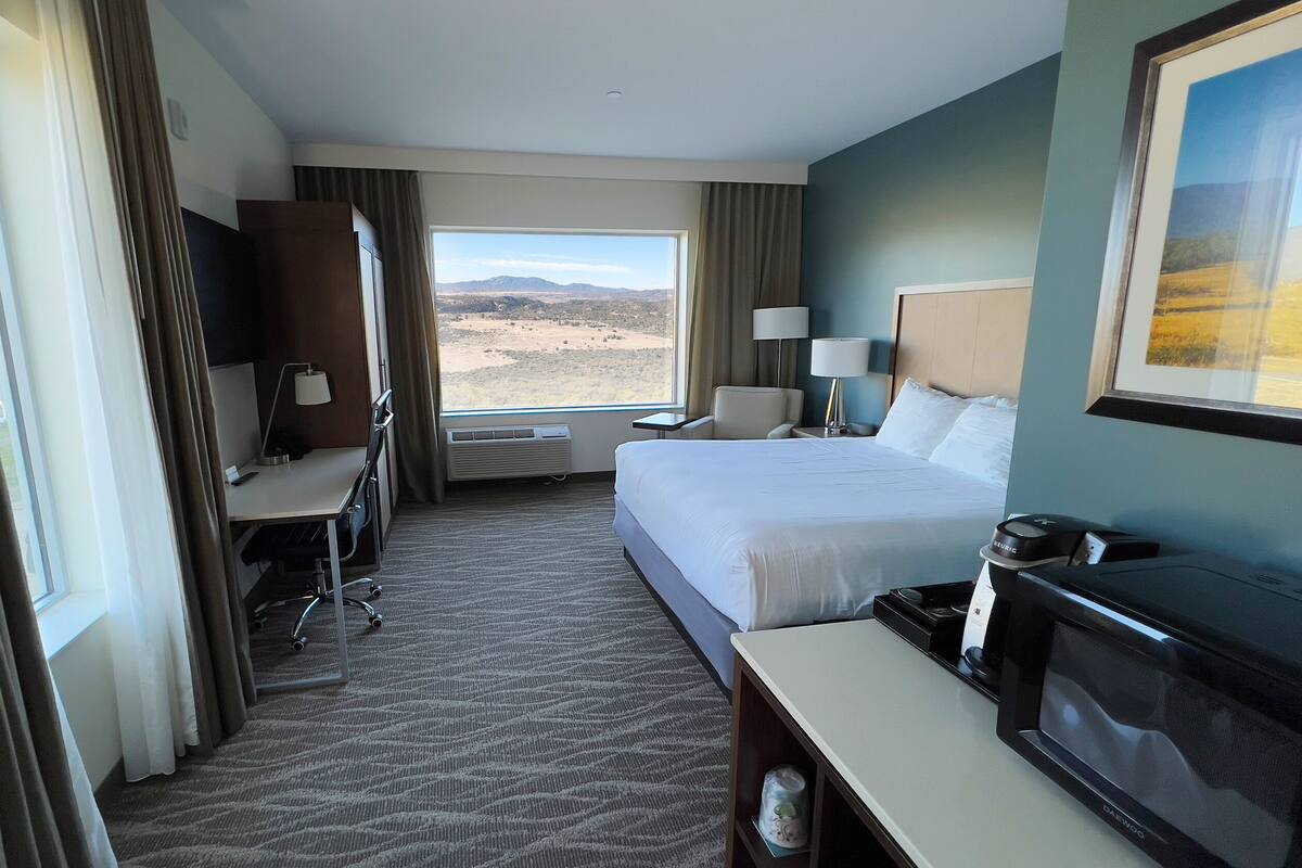 Ett hotellrum med en säng, ett skrivbord, en stol, en TV och utsikt över ett ökenlandskap.