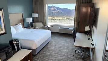Habitación de hotel con una cama grande, un escritorio, una silla, un televisor y vistas a las montañas.