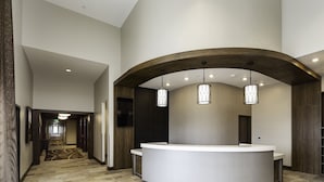 A reception area with a curved reception desk, a patterned carpet, and a hallway leading to an elevator.