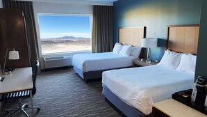 A hotel room with two beds, a desk, a chair, a coffee maker, and a view of a desert landscape.