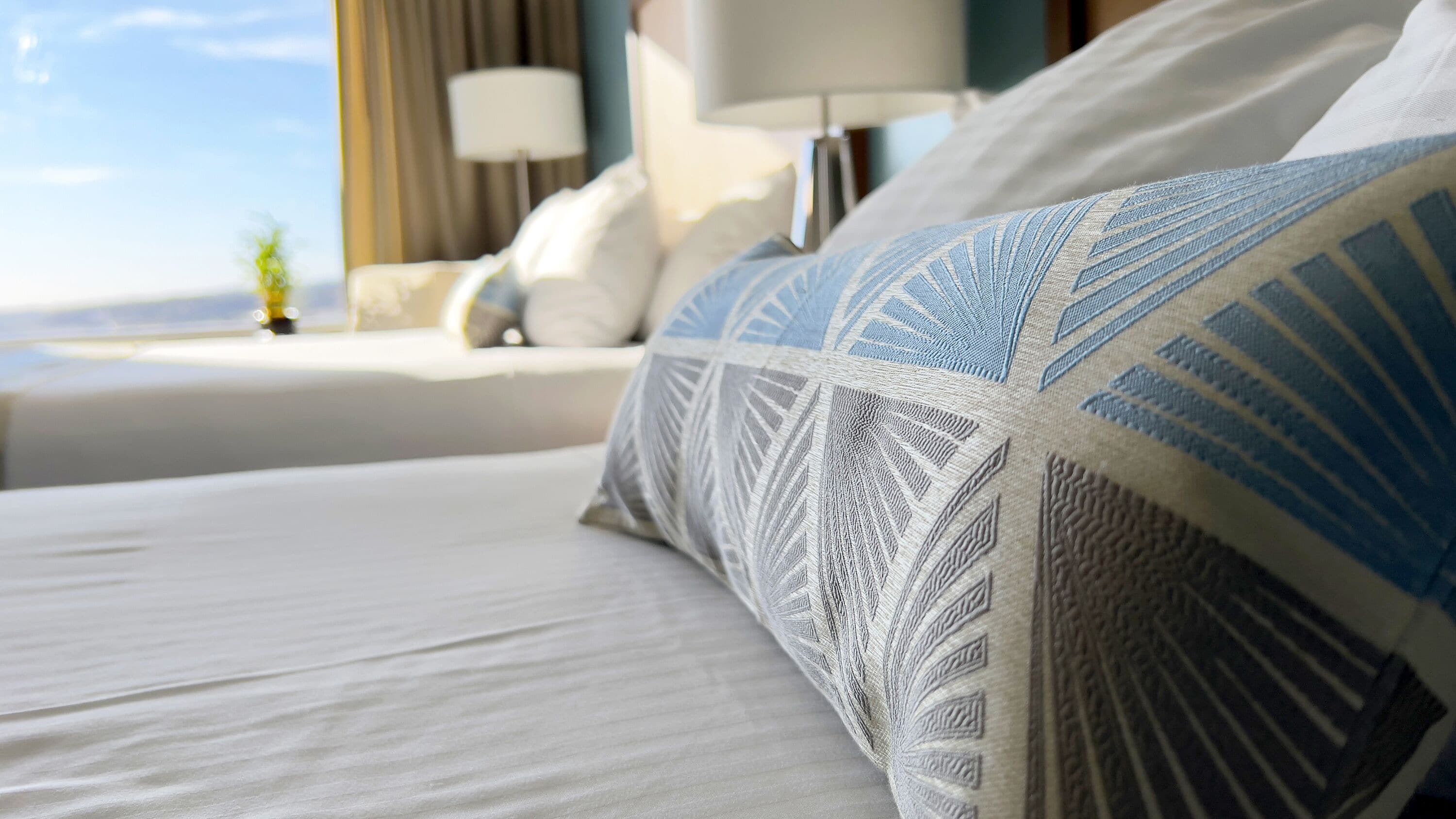 Una cama bien hecha con almohadillas estampadas y vistas a un paisaje urbano a través de una ventana.