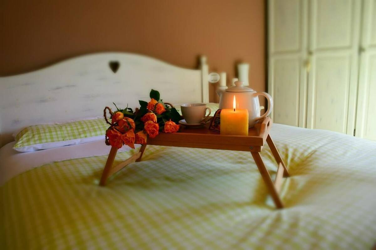 A bed with a checkered bedspread, a bedside table with a candle, a teapot, and a cup.