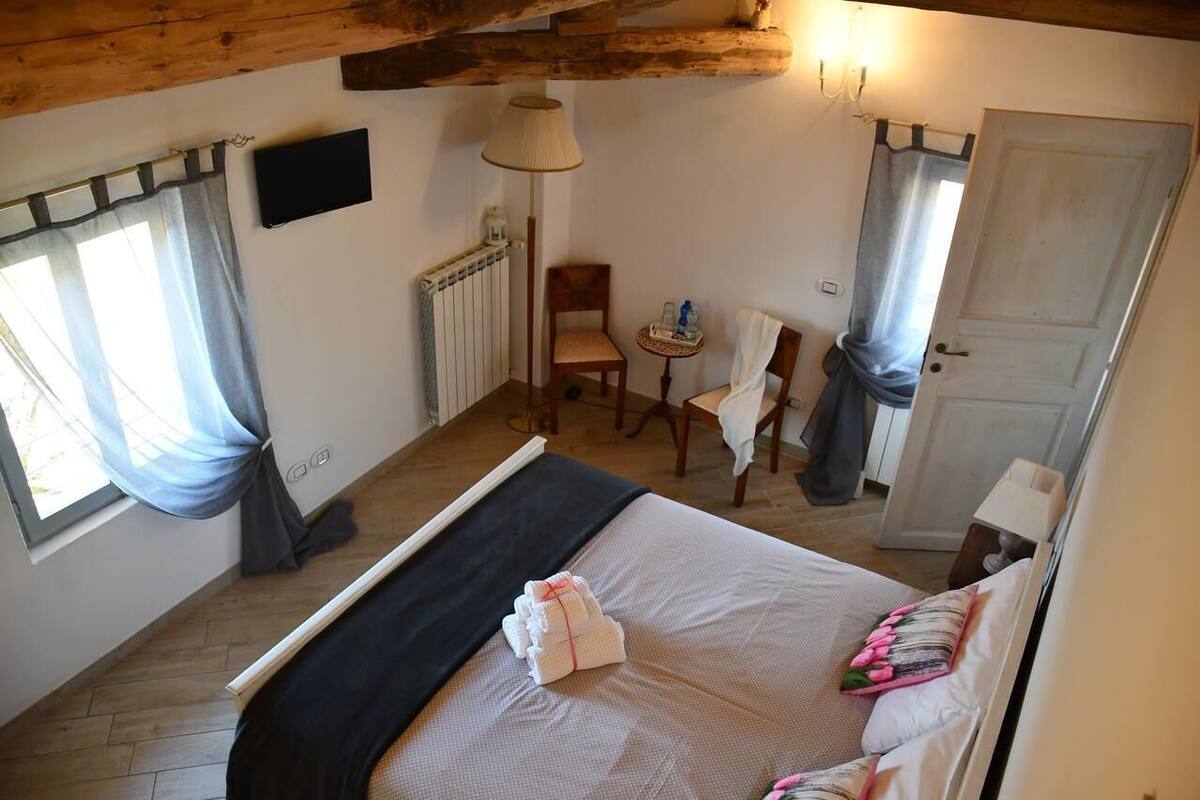 A bedroom with a bed, a chair, a small table, a radiator, a TV, and a door.