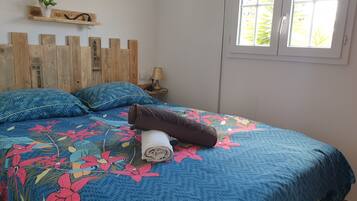A bedroom with a wooden headboard, a floral bedspread, and a window with a view of greenery.