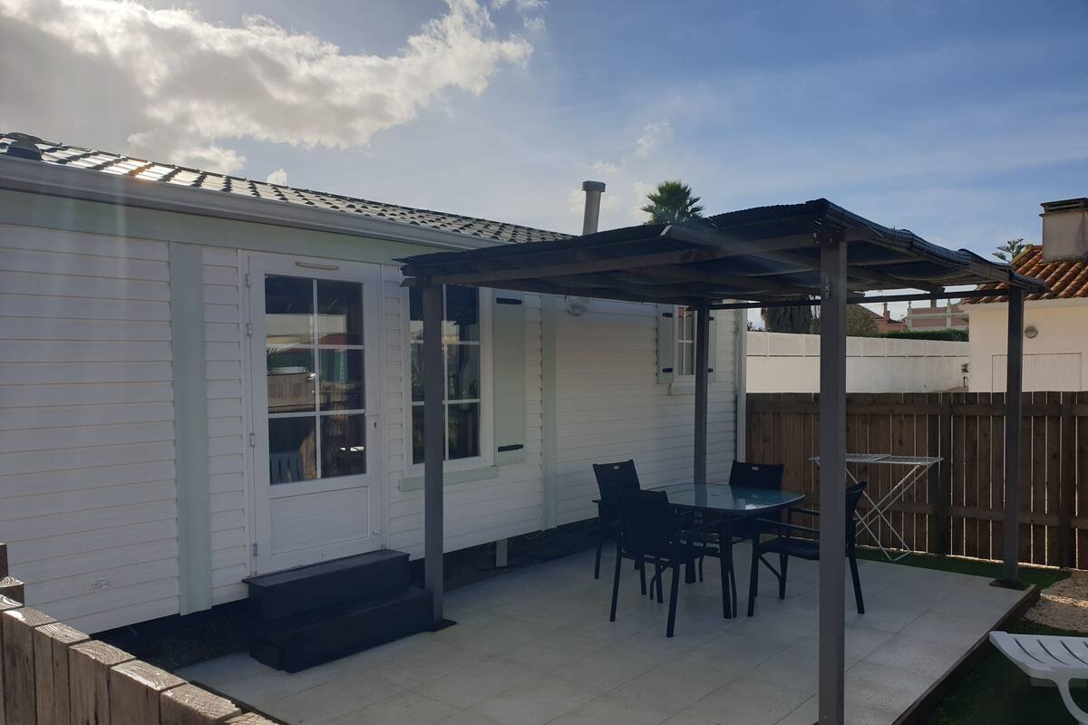 Une terrasse avec une table et des chaises, un espace salon couvert et une clôture en bois.