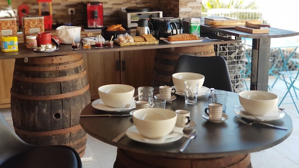 Un comedor rústico con barriles de madera como sillas, una mesa dispuesta con cuencos, tazas y diversos alimentos.