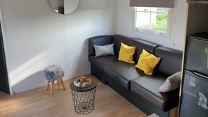 Una sala de estar moderna con un sofá gris oscuro, dos cojines amarillos, un espejo redondo y una pequeña mesa redonda con adornos.