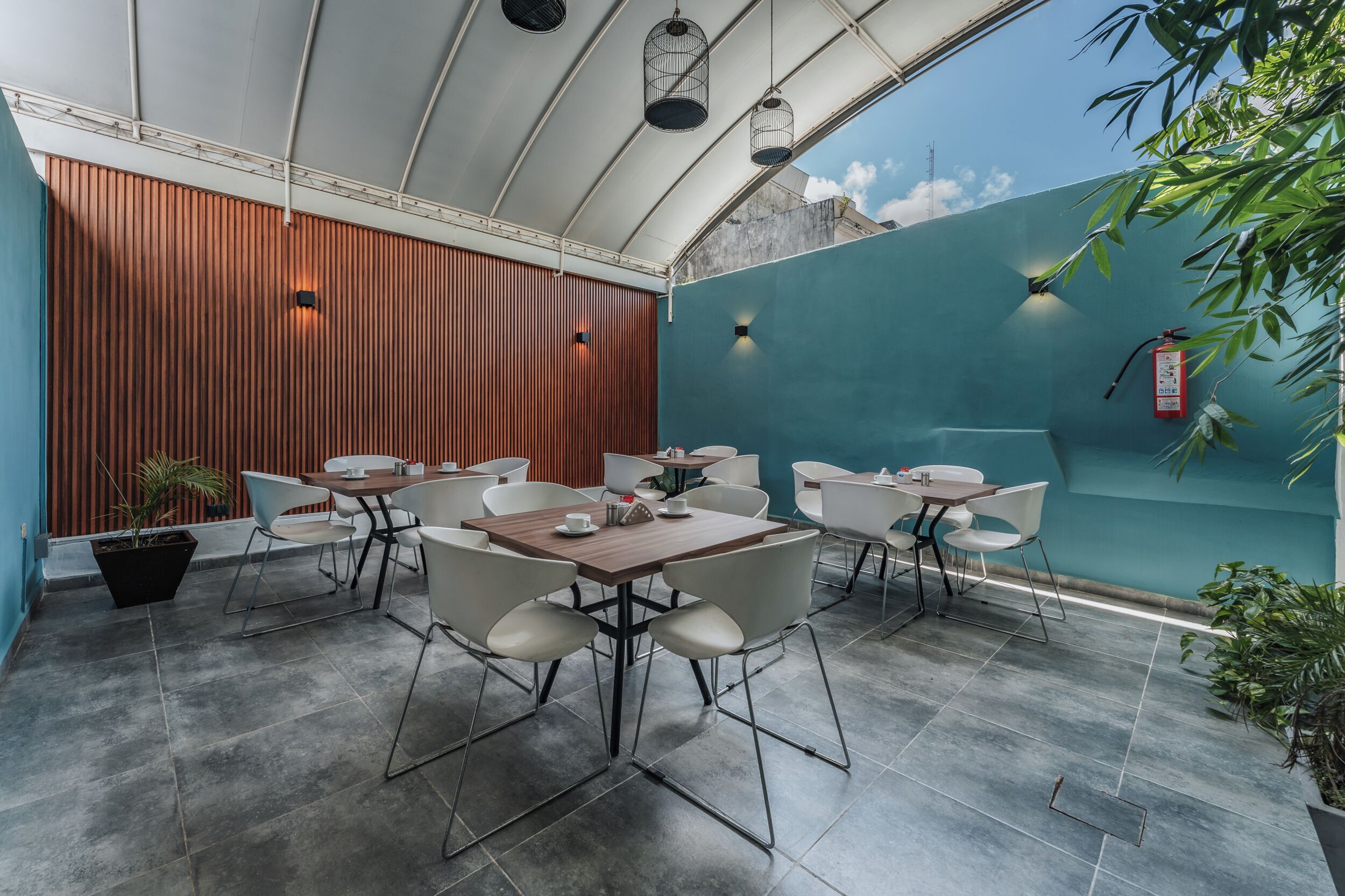 A modern outdoor dining area with tables and chairs, a fire extinguisher, and potted plants.