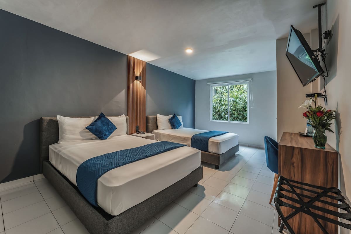 A modern hotel room with two beds, a large window, and a TV mounted on the wall.