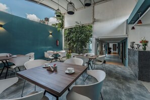 A modern cafe with wooden tables and white chairs, a blue wall, and a view of the sky.