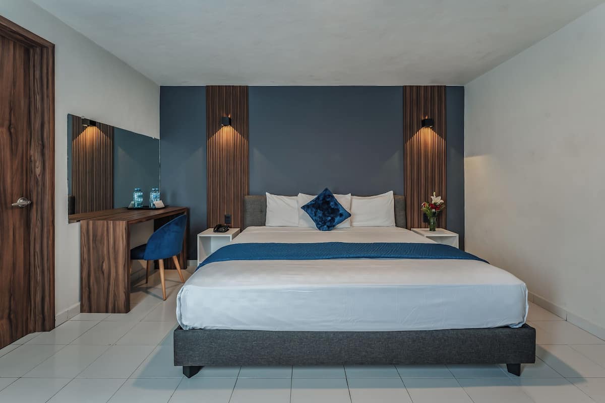 A modern bedroom with a large bed, a desk, and a chair. There are two bedside tables with lamps.