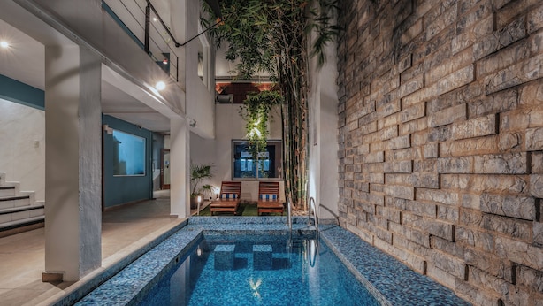 An indoor swimming pool with a tiled blue floor, a brick wall on one side, and a seating area with chairs and a table. - Hotel Casa Nova Mérida (Mérida)