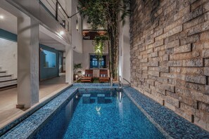 An indoor swimming pool with a tiled blue floor, a brick wall on one side, and a seating area with chairs and a table. - Hotel Casa Nova Mérida (Mérida)