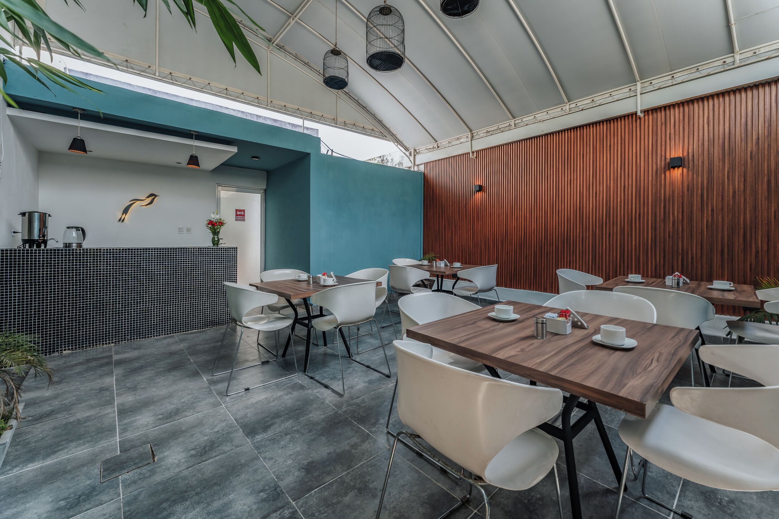 A modern outdoor dining area with tables and chairs, a blue accent wall, and a wooden panel wall.