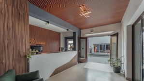 A modern reception area with a wooden accent wall, a curved reception desk, and a potted plant. - Hotel Casa Nova Mérida (Mérida)