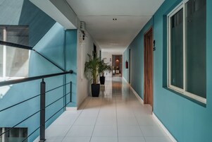 Un pasillo con paredes verde azulado, una escalera con barandales negros y plantas en macetas.