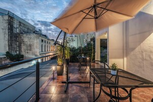 Un patio al aire libre con una mesa, sillas, un paraguas grande y plantas en macetas.