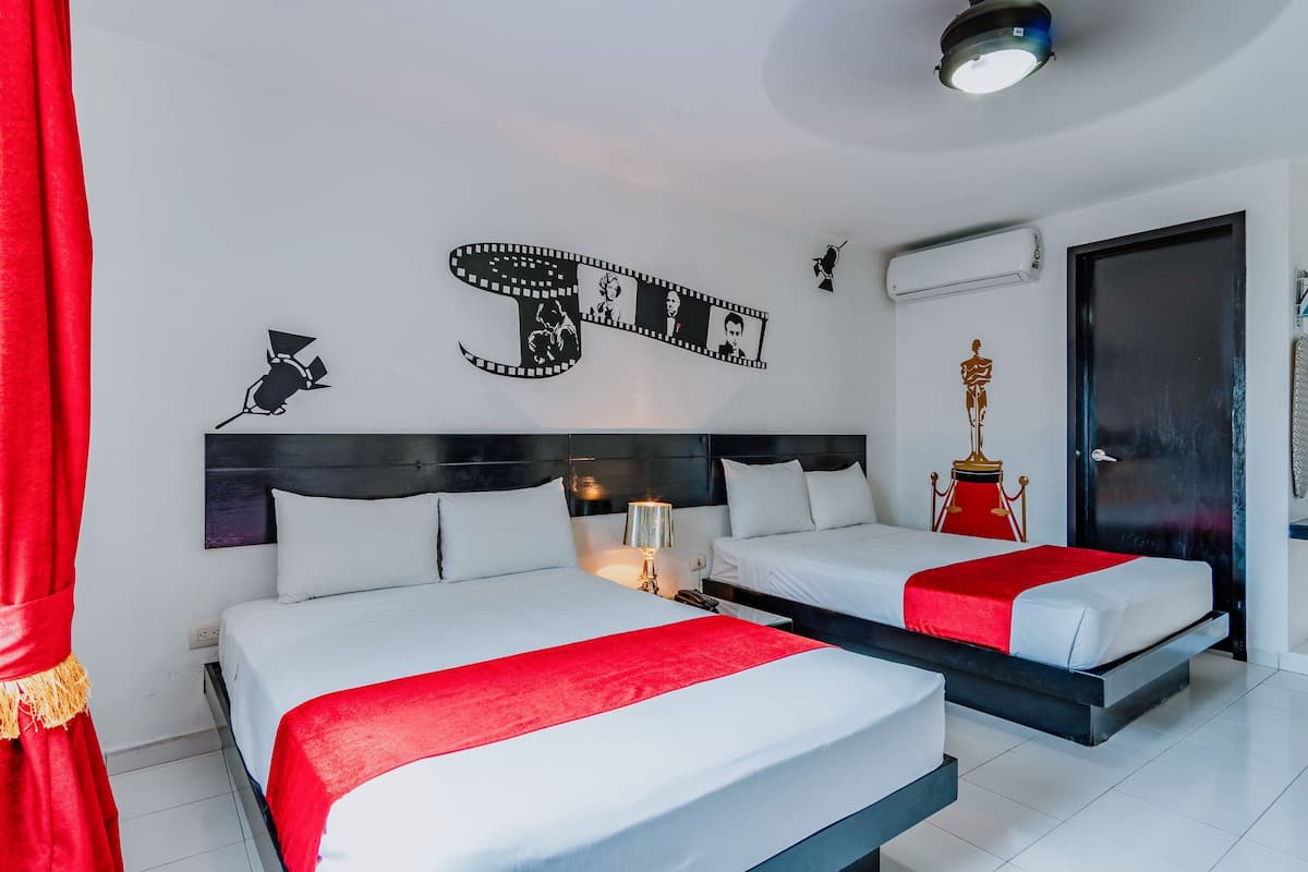 A hotel room with two beds, a red curtain, a filmstrip artwork, a trophy, and an air conditioning unit.