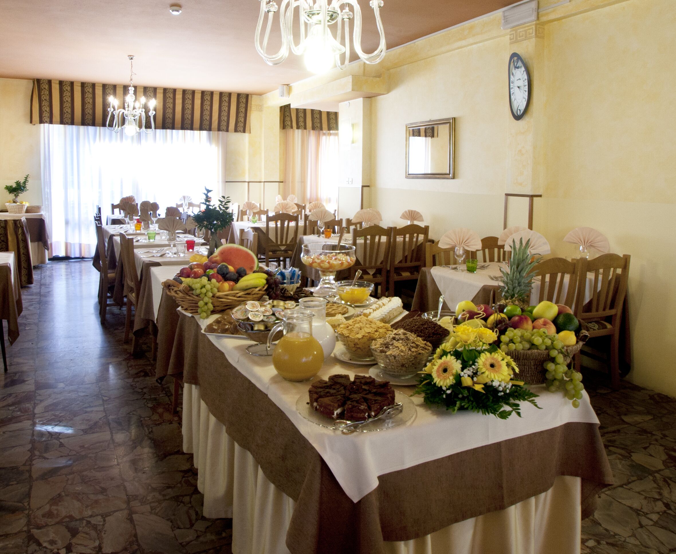 A dining area with multiple tables set for a meal, featuring a variety of food items and a clock on the wall.