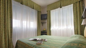 Una habitación de hotel con una cama, un televisor en la pared y una ventana con cortinas.