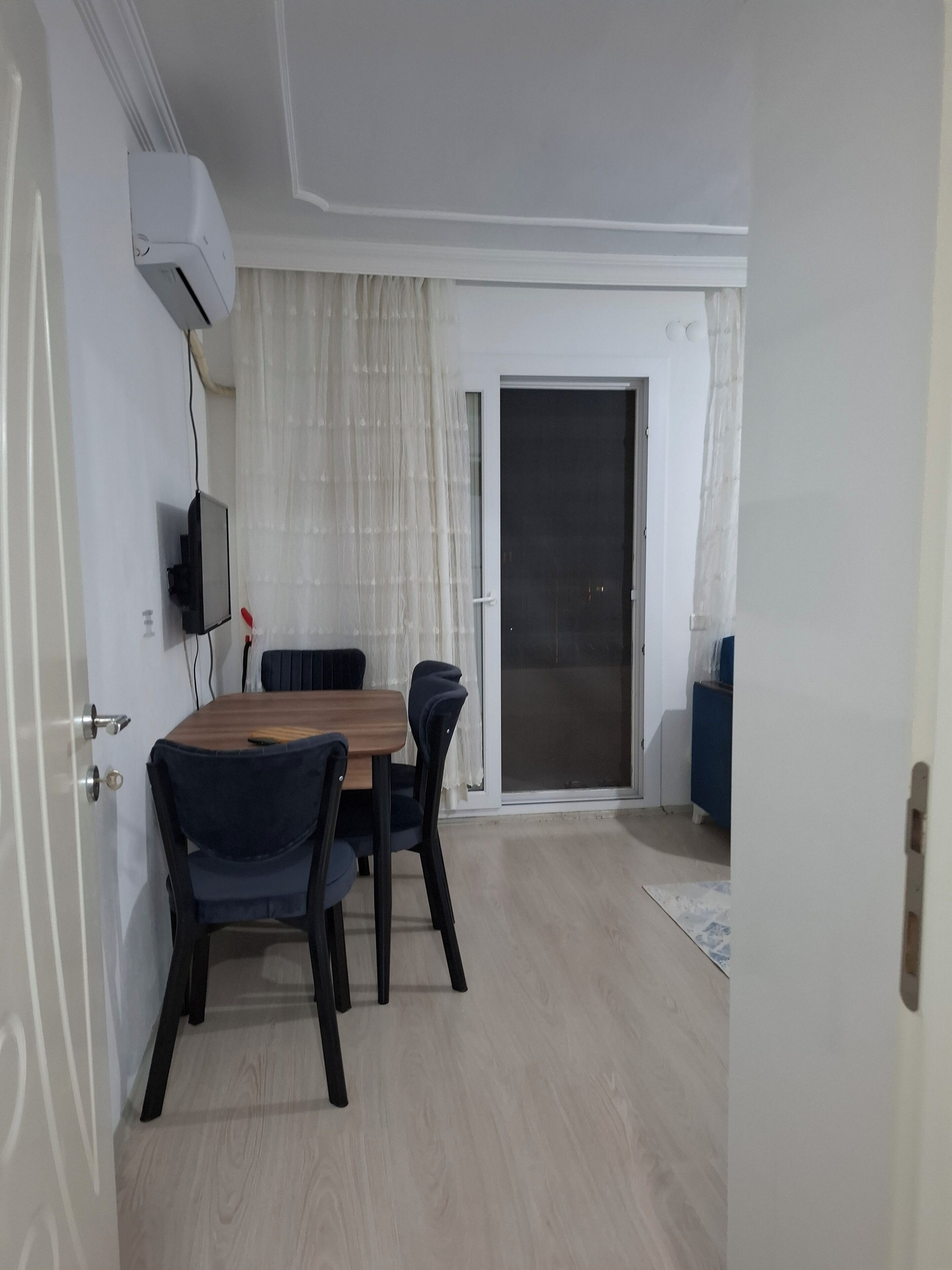 Una habitación con mesa de comedor, sillas, un televisor montado en la pared y un ventanal corredero que da a un espacio exterior.