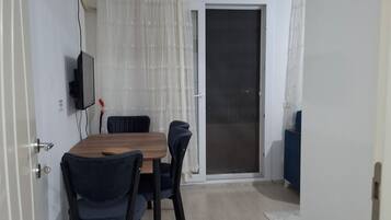 Una habitación con mesa de comedor, sillas, un televisor montado en la pared y un ventanal corredero que da a un espacio exterior.