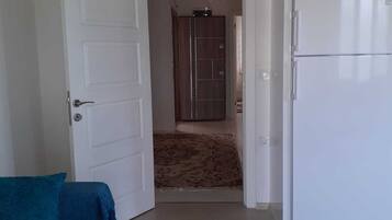 A room with a white door, a blue sofa, a white refrigerator, and a shower area in the background.