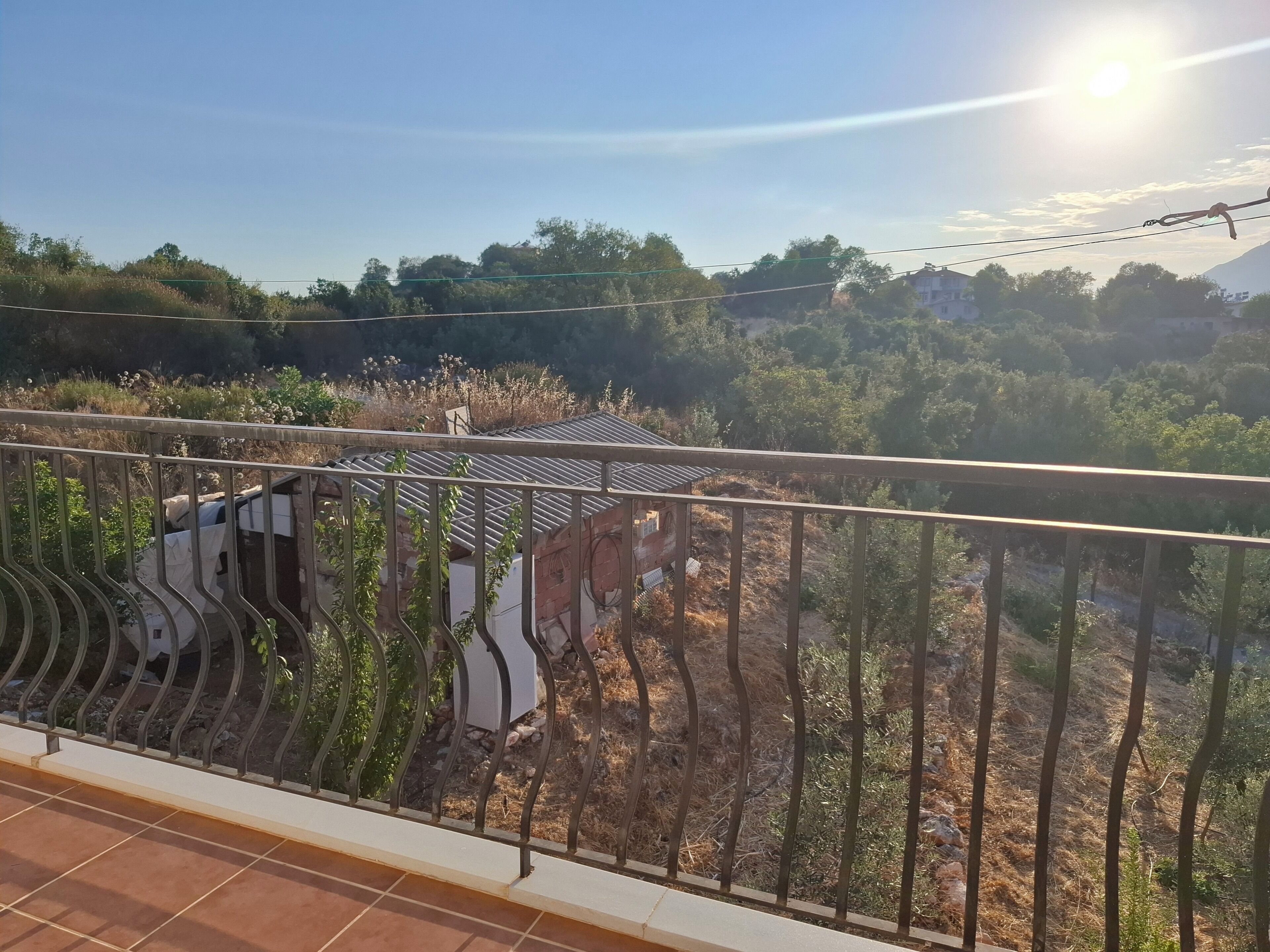 A balcony with a metal railing, overlooking a residential area with houses and trees.