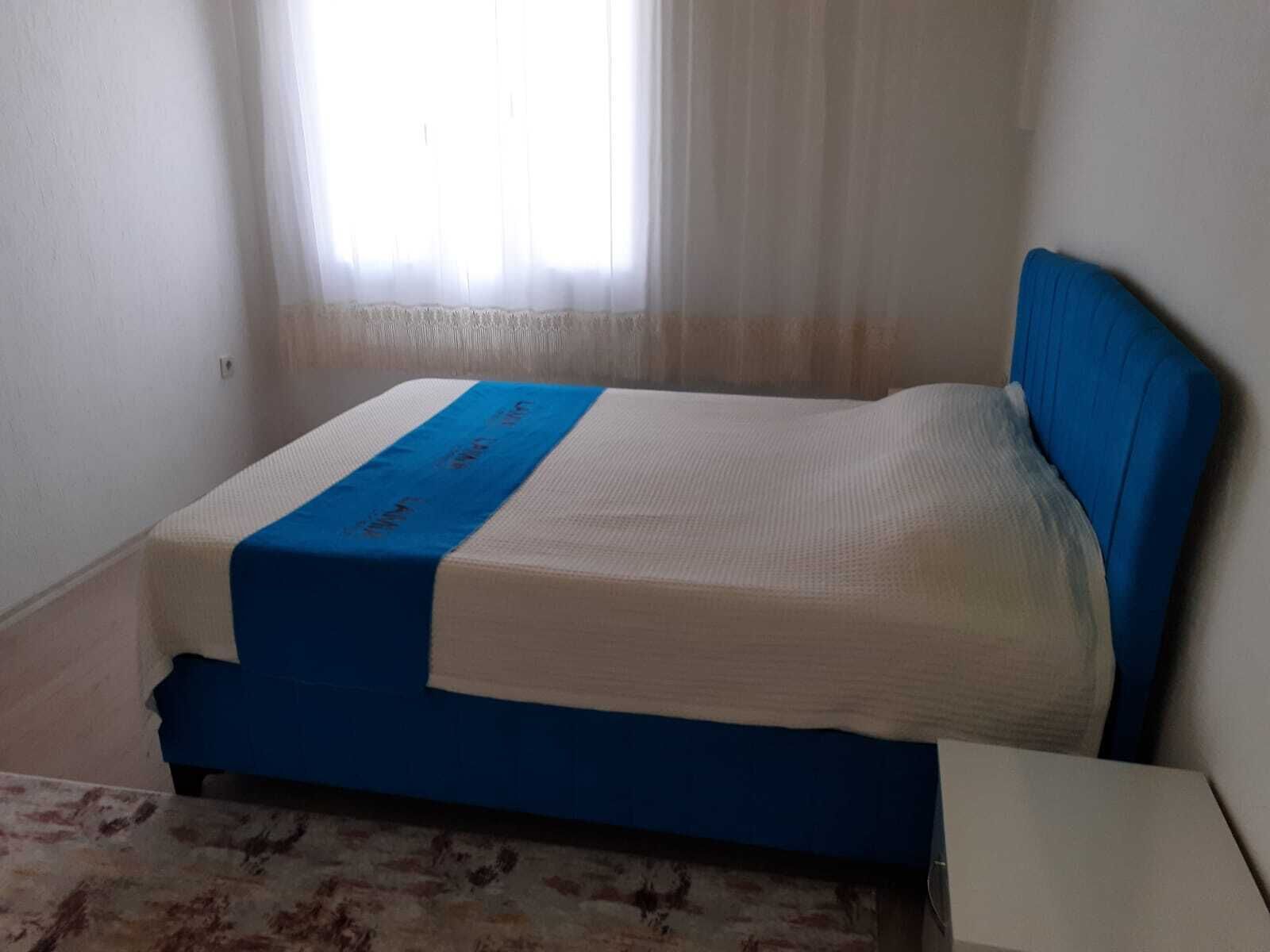 Una habitación pequeña con cama individual, cabecera azul y colcha blanca.