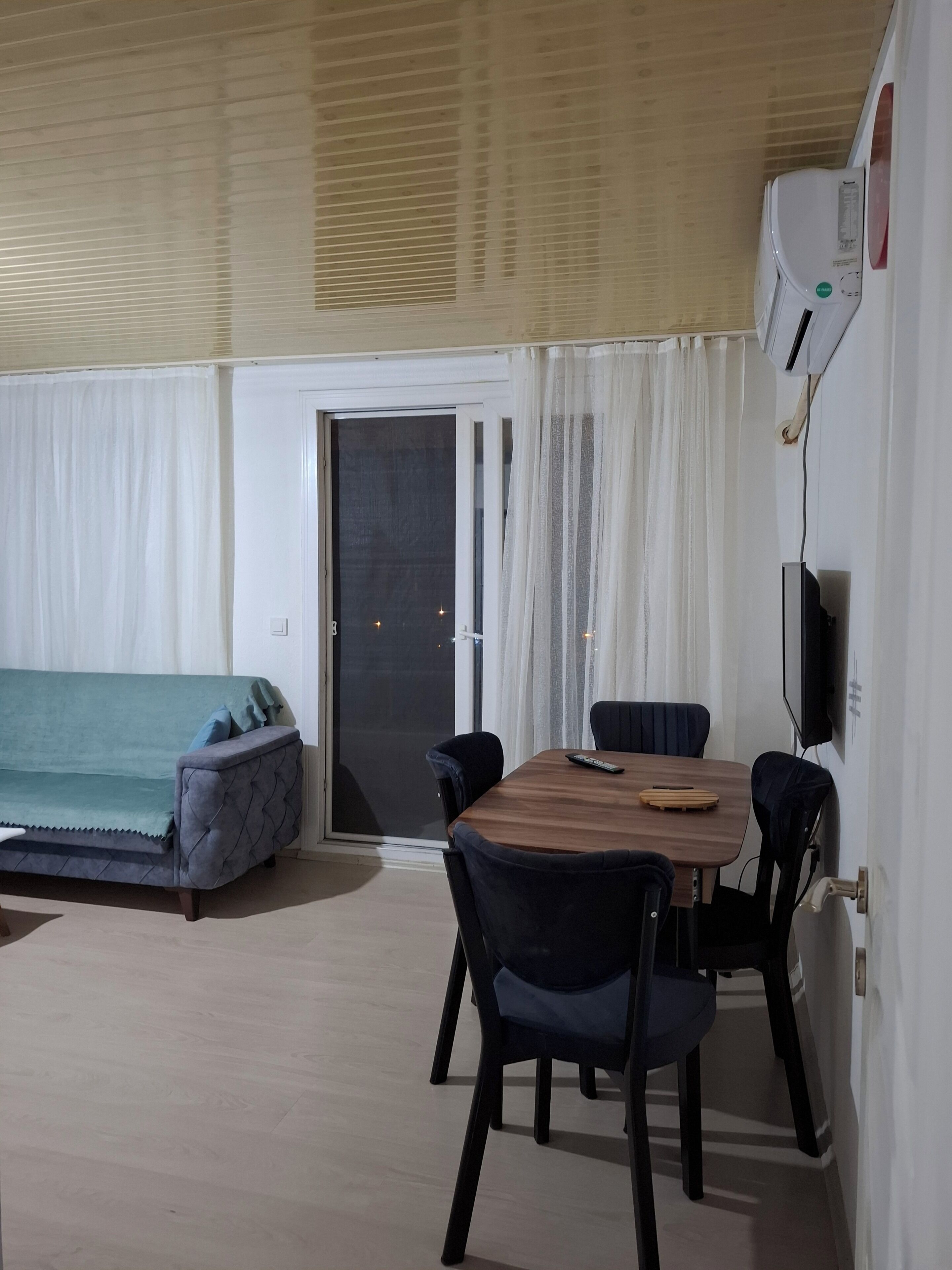 Et værelse med et træbord, fire stole, en sofa, en skydedør af glas og en vægmonteret aircondition.