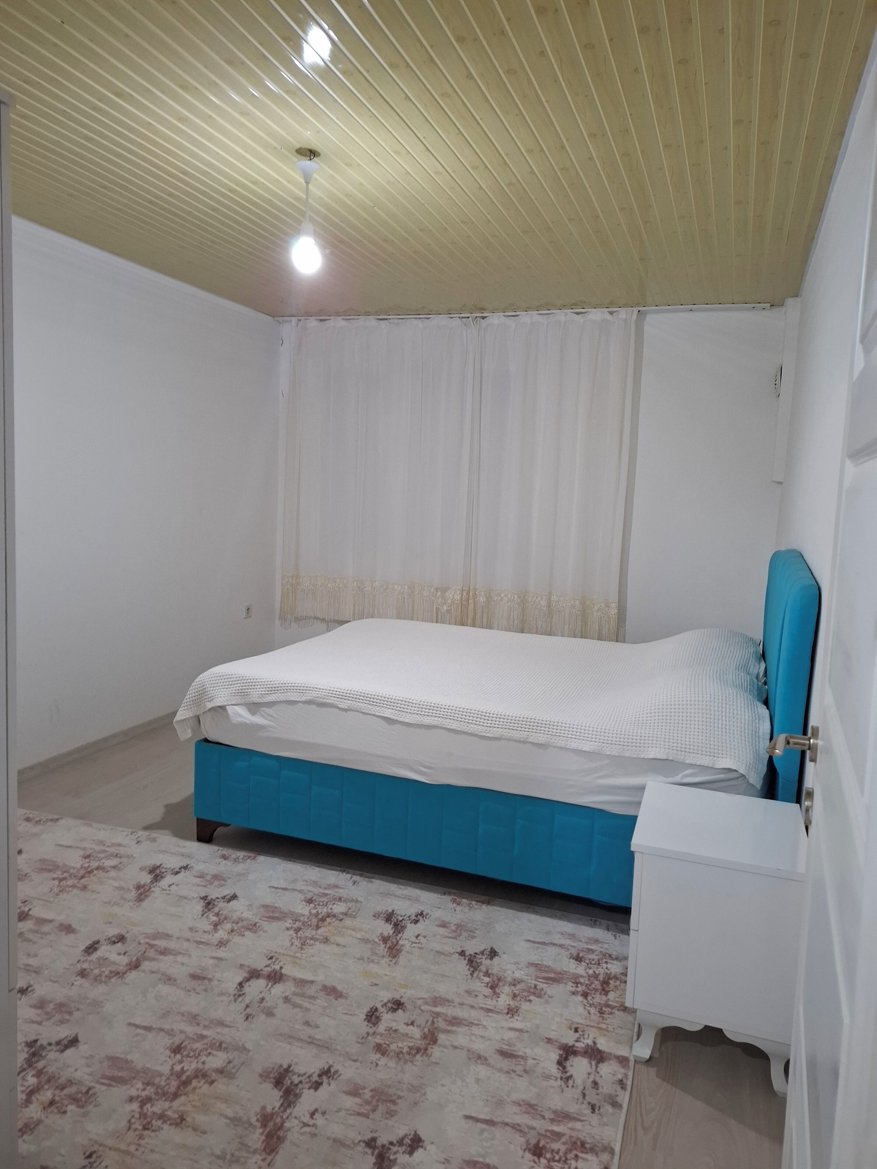 A bedroom with a bed, a nightstand, a ceiling fan, and a window with curtains.