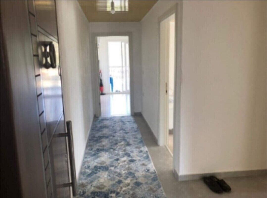 Un pasillo con alfombra estampada, una escalera metálica y un par de zapatos en el suelo.