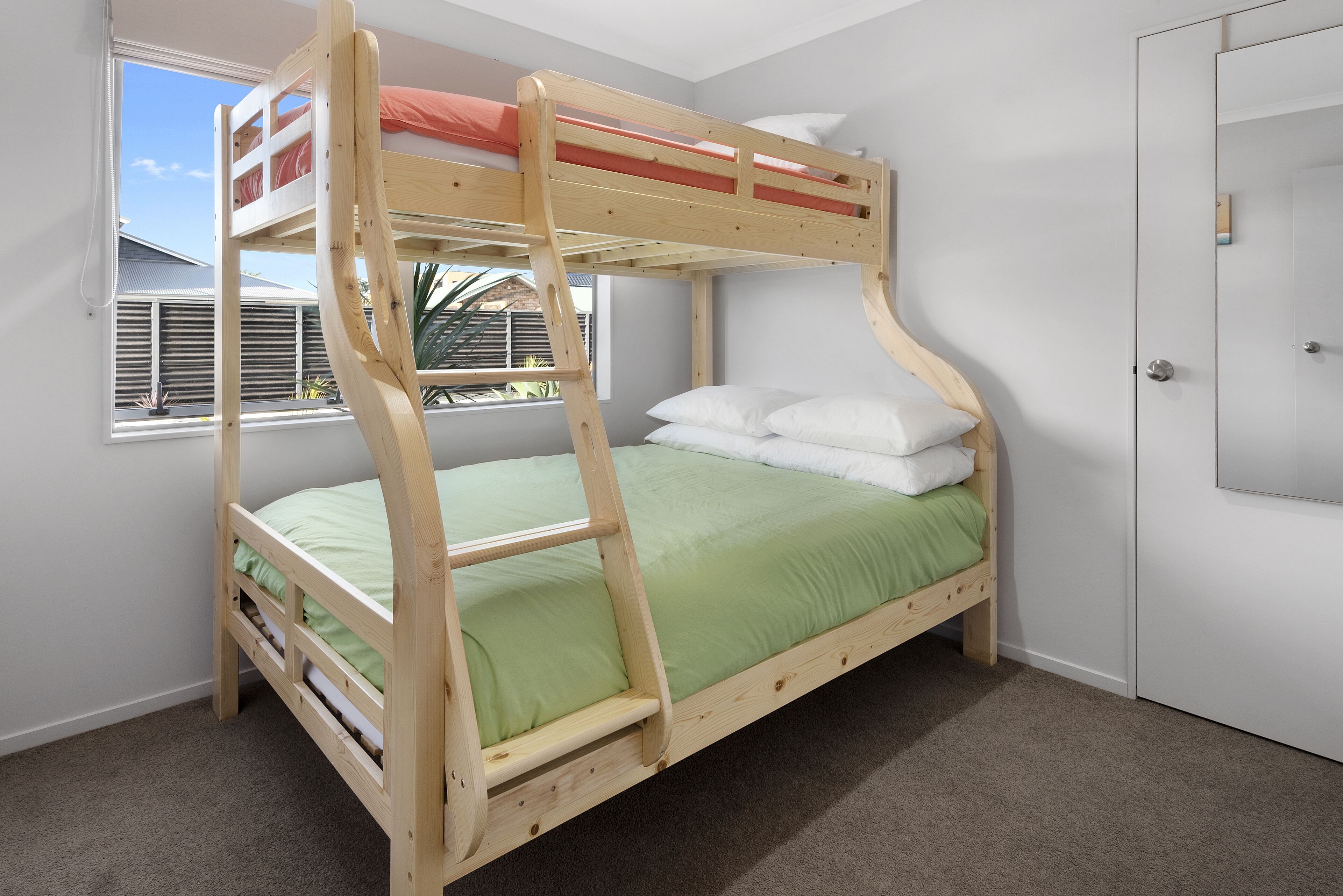 Ein Stockbett mit einer grünen Matratze, weißen Kissen und einem Holzrahmen.