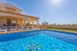 A swimming pool with lounge chairs, a covered patio, and a view of the city skyline.